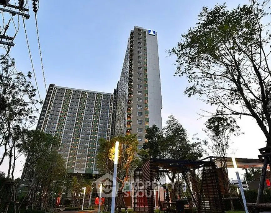 Modern high-rise residential building with lush green surroundings and clear sky.