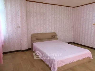 Cozy bedroom with wooden flooring and floral wallpaper, featuring a simple bed setup for a serene ambiance.