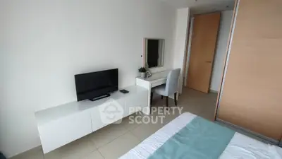 Modern bedroom with TV and desk, featuring minimalist decor and natural light.