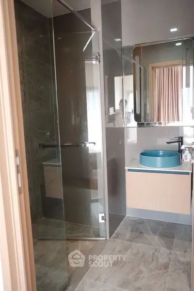 Modern bathroom with glass shower and stylish blue basin in contemporary apartment.