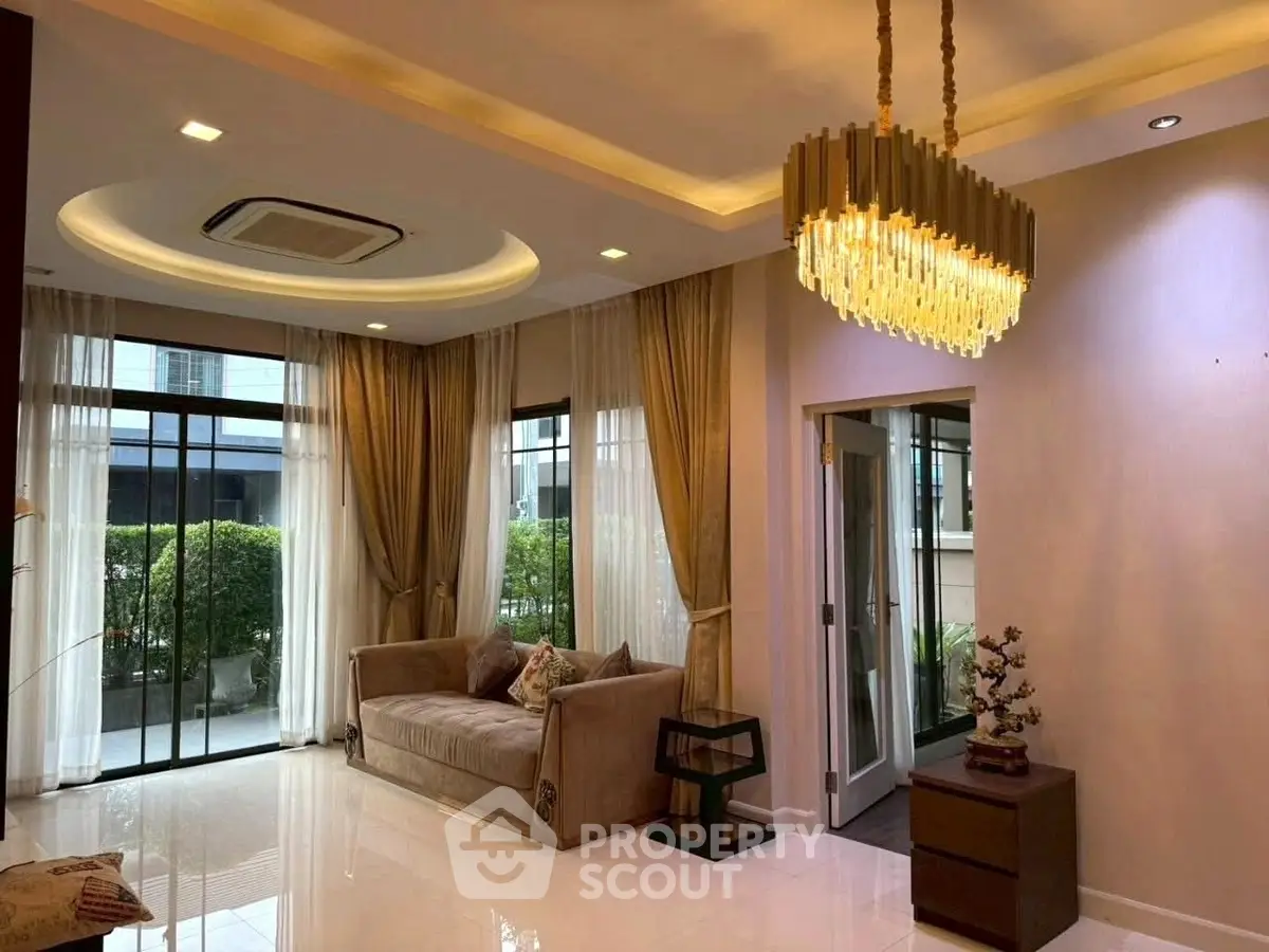 Luxurious living room with elegant chandelier and large windows, offering a serene garden view.