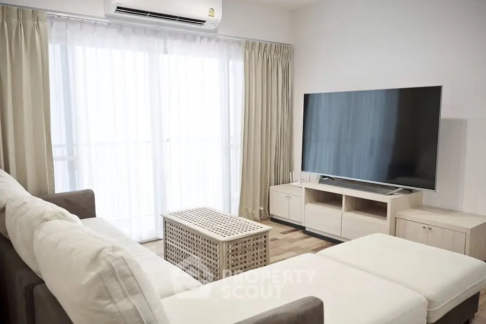 Modern living room with large TV and comfortable seating in a bright apartment.
