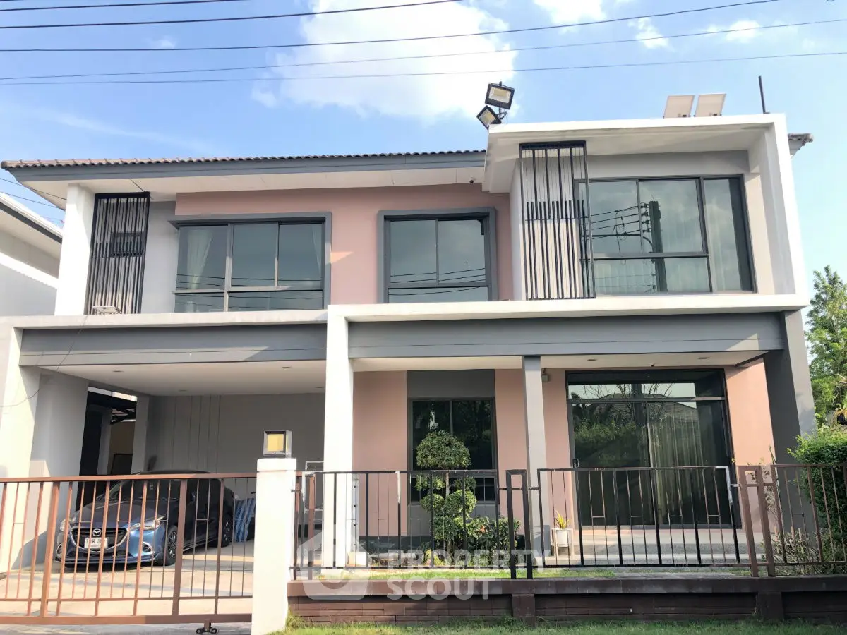 Modern two-story house with large windows and gated driveway in a suburban setting.