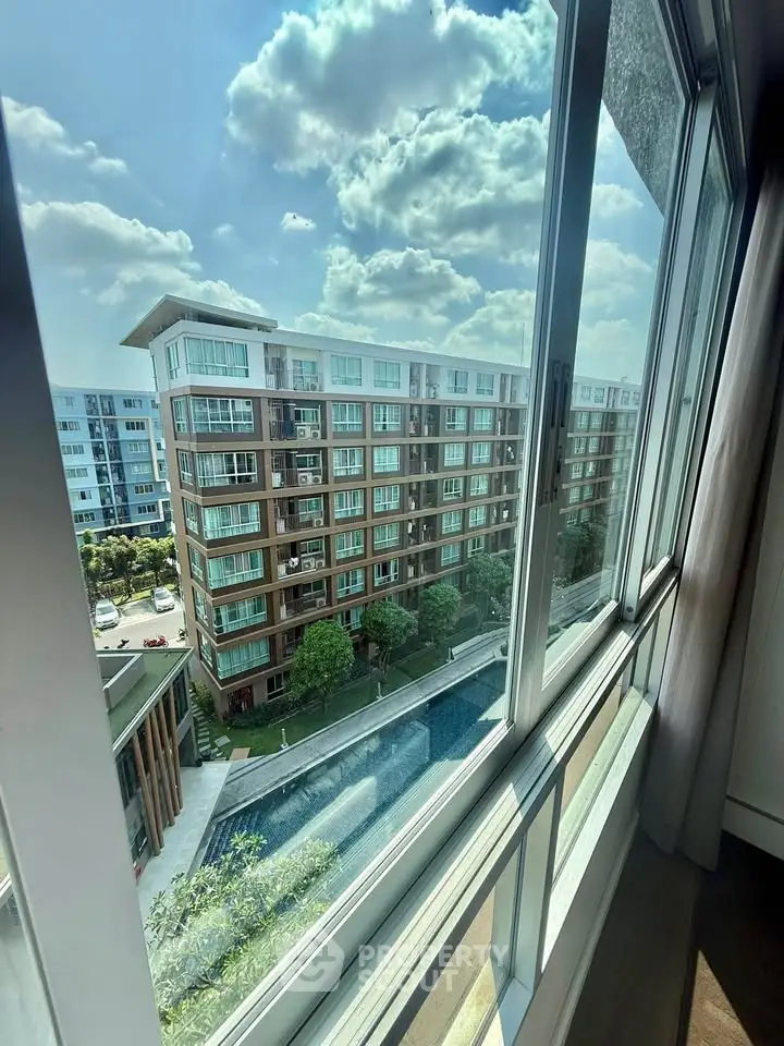 Stunning view from modern apartment window overlooking pool and residential complex.