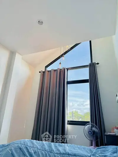 Bright bedroom with high ceiling and large window offering natural light and scenic view.