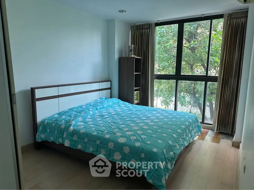 Cozy bedroom with large window and modern furnishings, offering a serene view of lush greenery.