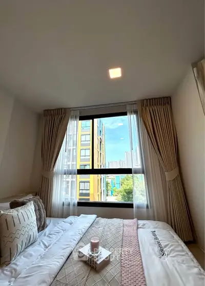 Cozy bedroom with large window offering city view, elegant curtains, and stylish bedding.