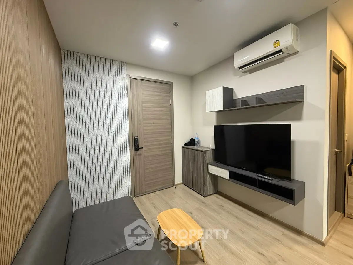 Modern living room with sleek furniture and wall-mounted TV, featuring wood accents and air conditioning.
