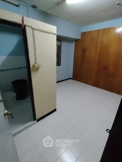 Spacious and versatile room with tiled flooring, large wooden wardrobe, and an attached bathroom, ideal for customization and personalization.