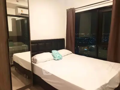 Cozy bedroom with city view, featuring a large window and modern decor.