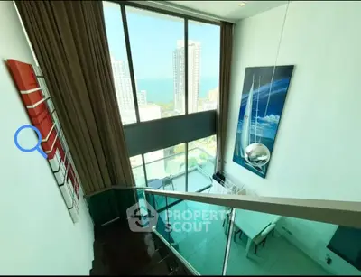 Stunning duplex with floor-to-ceiling windows and ocean view, featuring modern decor and elegant staircase.