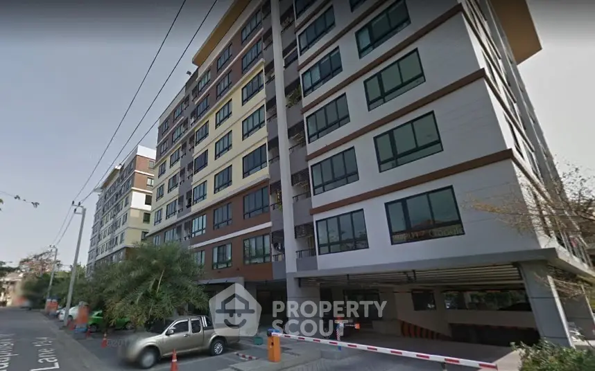 Modern multi-story residential building with street view and parking area.