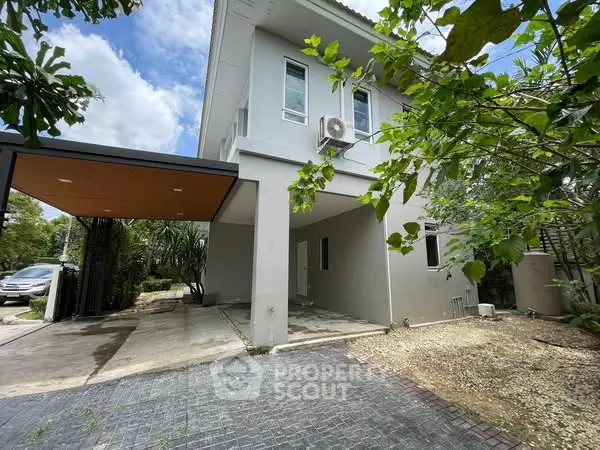 Modern two-story house with carport and lush greenery in a serene neighborhood.