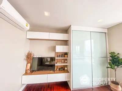 Modern minimalist living room with sleek built-in shelving, glossy white storage cabinets, and warm wooden flooring, complemented by natural light.