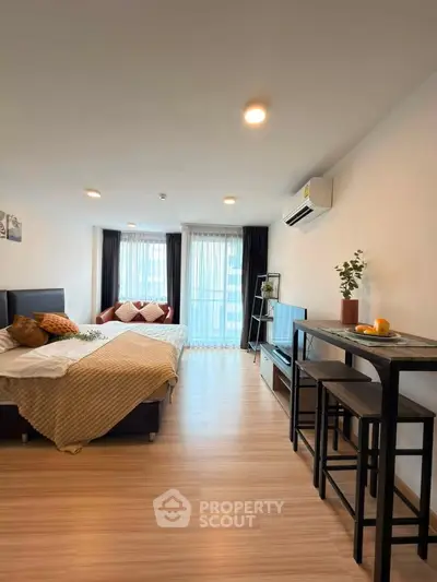 Modern studio apartment with cozy bed, stylish decor, and natural light from large windows.