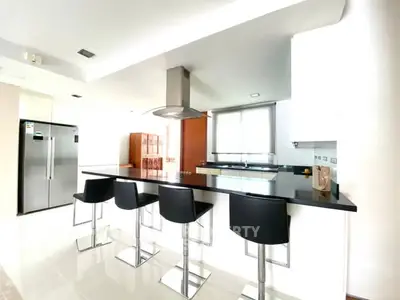 Modern kitchen with sleek black countertops and bar stools, featuring stainless steel appliances.