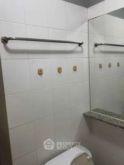 Compact bathroom with tiled walls and a large mirror, featuring a towel rack and hooks.