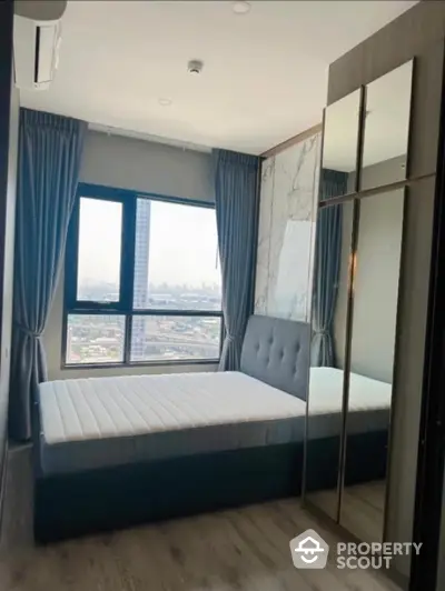 Modern bedroom with city view, featuring large window and mirrored wardrobe.