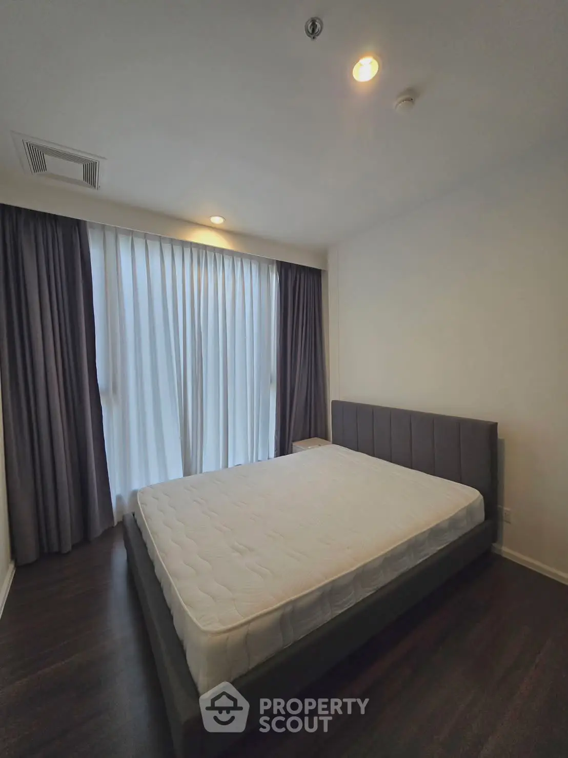 Spacious bedroom with large window and elegant dark curtains in modern apartment.