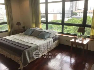Spacious bedroom with large windows offering a stunning city view, featuring elegant decor and hardwood floors.