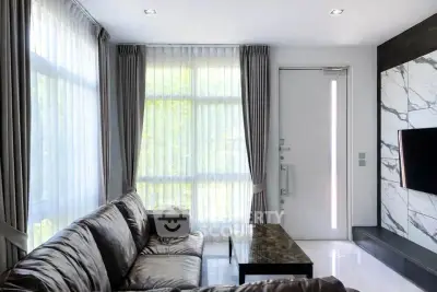 Modern living room with leather sofa, marble accent wall, and large windows with curtains.