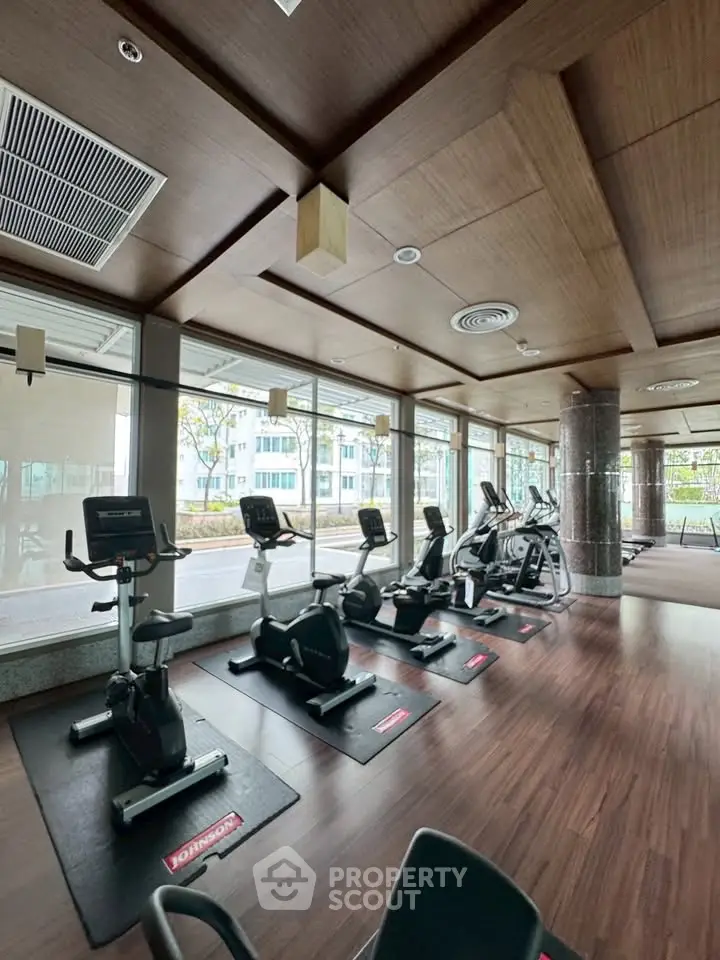 Spacious gym with modern exercise equipment and large windows offering natural light.