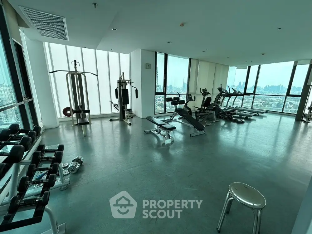 Spacious gym with modern equipment and panoramic city views in luxury high-rise building.