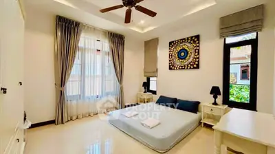 Spacious bedroom with elegant decor and natural light, featuring a ceiling fan and stylish window treatments.