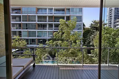 Spacious balcony with modern railing overlooking lush greenery and contemporary apartment building.
