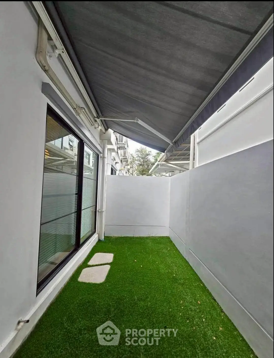 Charming outdoor space with artificial grass and modern awning, perfect for relaxation and privacy.