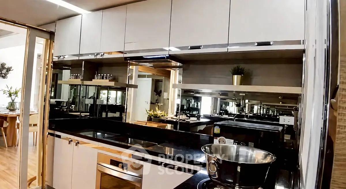 Modern kitchen with sleek cabinetry and built-in appliances, featuring a reflective backsplash and elegant decor.