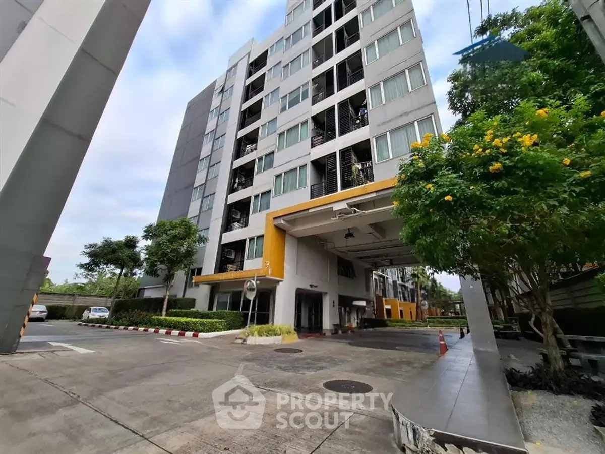 Modern high-rise building with lush greenery and spacious parking area.