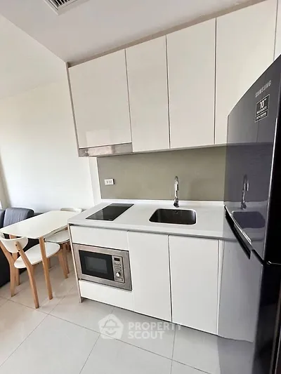 Modern kitchen with sleek white cabinets, built-in microwave, and Samsung fridge in a cozy apartment.