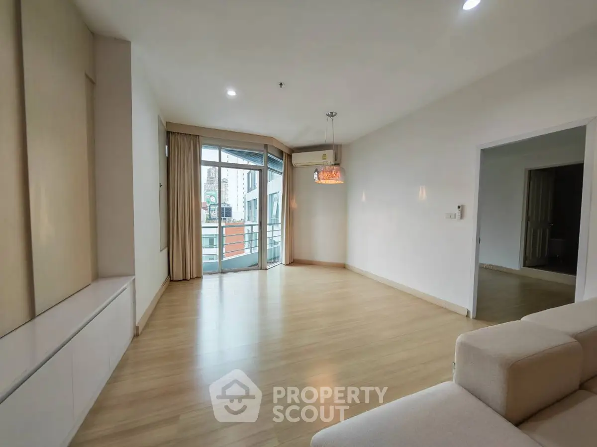 Spacious modern living room with wooden flooring and large windows in a contemporary apartment.