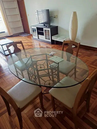 Charming dining area with glass table and wooden chairs, featuring parquet flooring and modern TV setup.