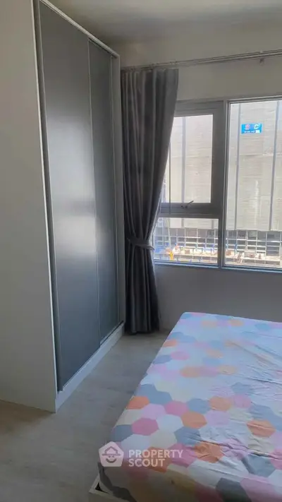 Cozy bedroom with large window and modern wardrobe in urban apartment.