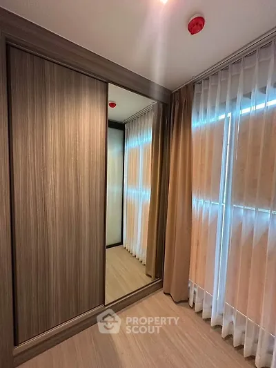 Spacious bedroom with elegant wooden wardrobe and large windows with sheer curtains.