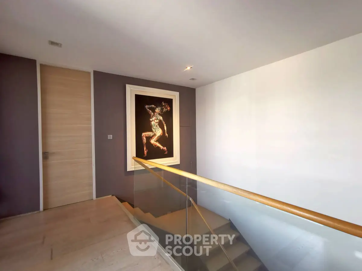 Modern staircase with elegant artwork and wooden railing in a stylish home interior.