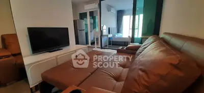 Modern living room with leather sofa and flat-screen TV, adjacent to a cozy bedroom.