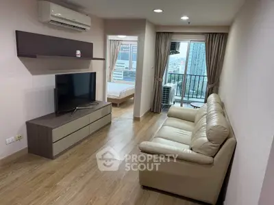Modern living room with leather sofa, TV, and view of bedroom and cityscape from balcony.