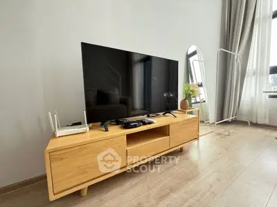 Modern living room with sleek wooden TV stand and large flat-screen TV, bright natural light.