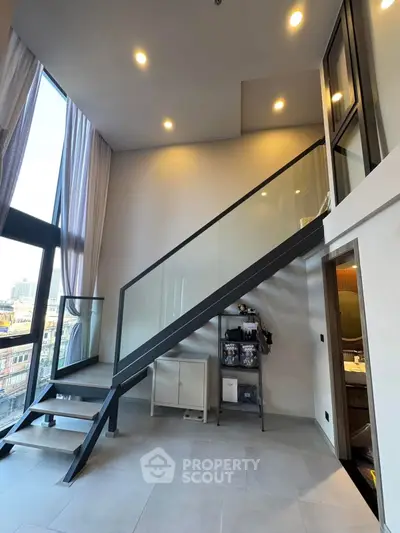 Modern loft apartment with high ceilings and sleek staircase, featuring large windows and stylish interior design.