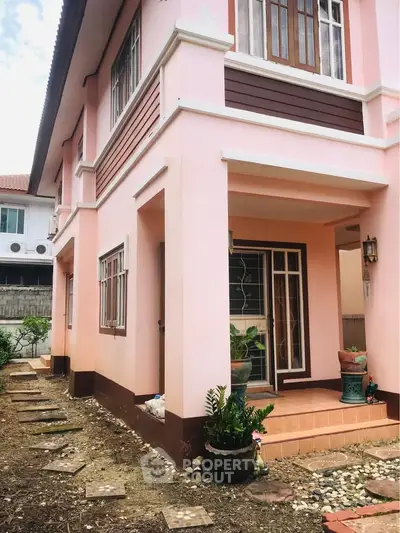 Charming pink two-story house with inviting entrance and potted plants, perfect for family living.