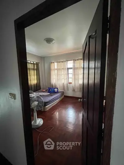 Cozy bedroom with wooden flooring and natural light through large windows.