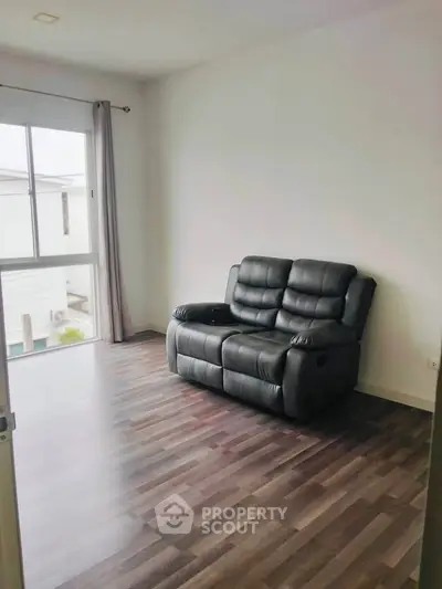 Spacious living room with sleek wooden flooring and cozy black leather sofa.