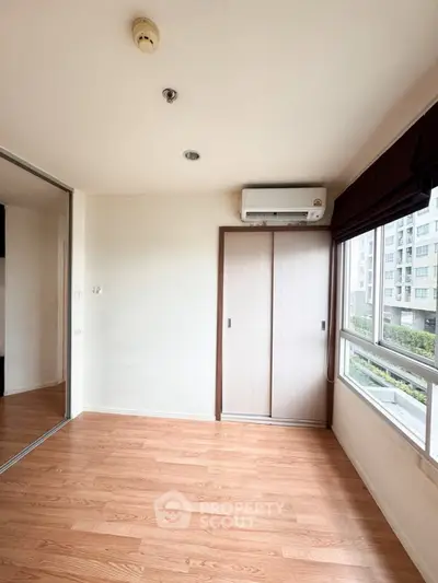 Spacious bedroom with wooden flooring and large window offering city view