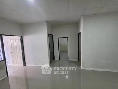 Spacious empty room with glossy tiled floor and multiple doorways, ideal for customization.