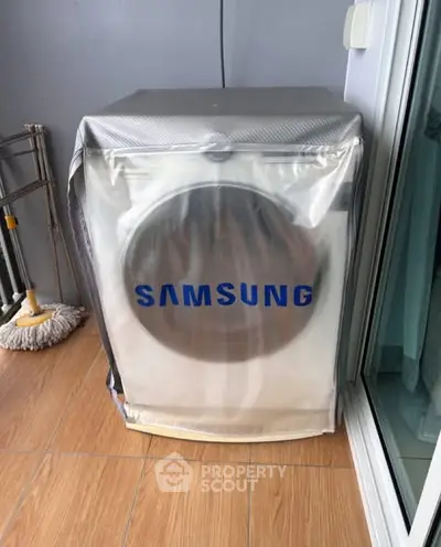 Modern Samsung washing machine on a tiled balcony with sliding glass door.