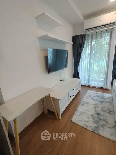 Modern living room with wall-mounted TV and stylish furniture, featuring large window with natural light.