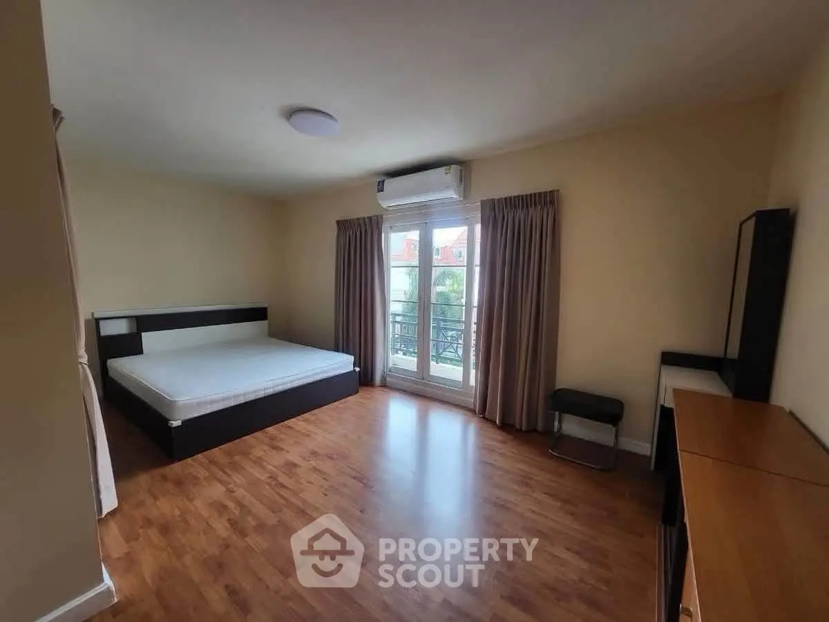 Spacious bedroom with wooden flooring and large window for natural light